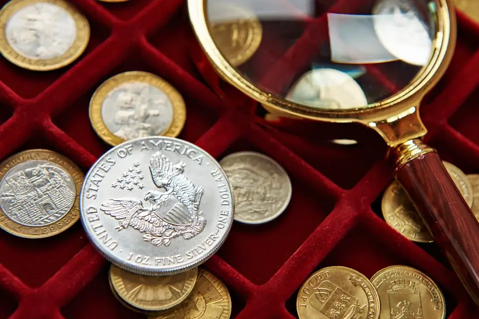 A silver American Eagle and other coins resting in a red velvet tray next to a magnifying glass