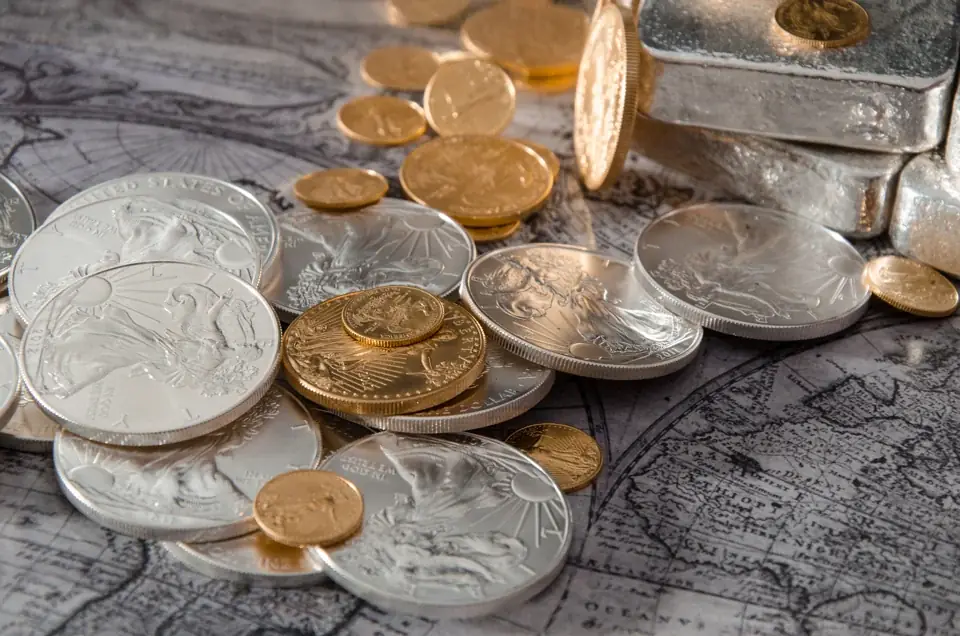 American Silver Eagles and small gold Eagles scattered on a vintage map beside a stack of poured silver bars