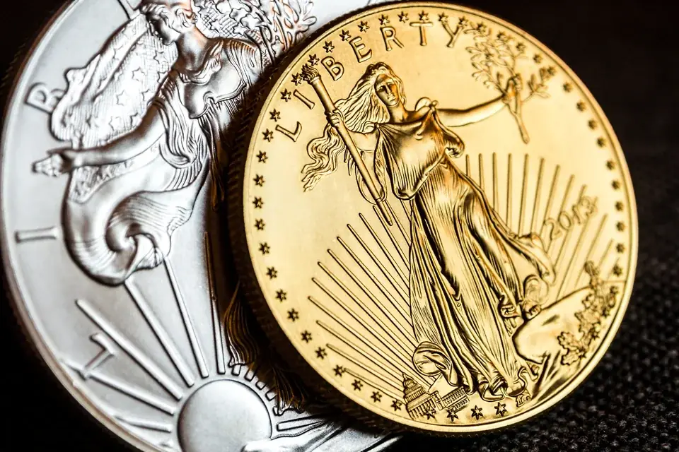 A gold American Eagle coin leaning against a silver American Eagle, close up